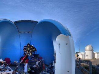 an open sided dome structure hovers above telescope equipment in the foreground. behind to the right, a domed silo with blue skies above.